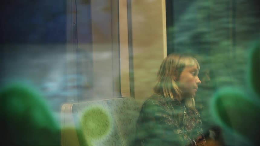 A woman sitting on a bus looks out the window as people walk down the aisle