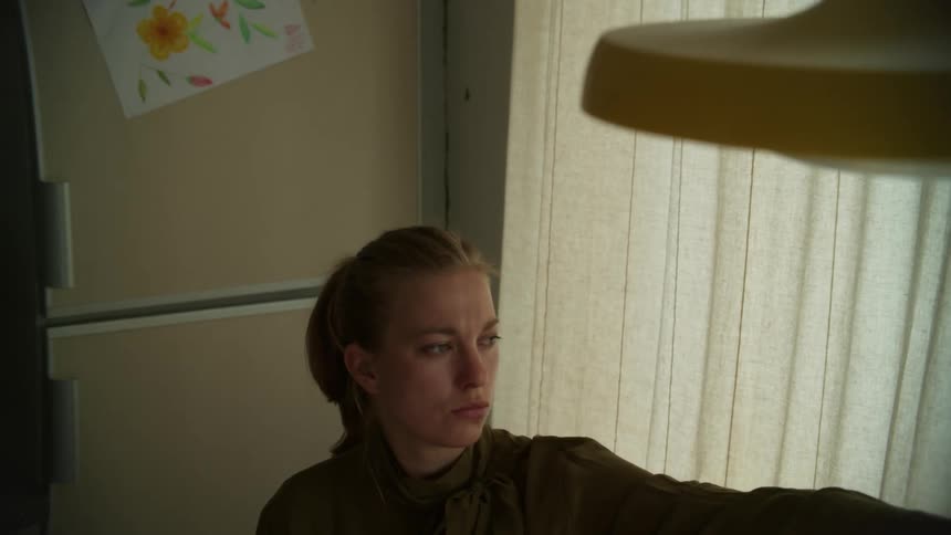 Woman closes the curtains of a window on the kitchen at home