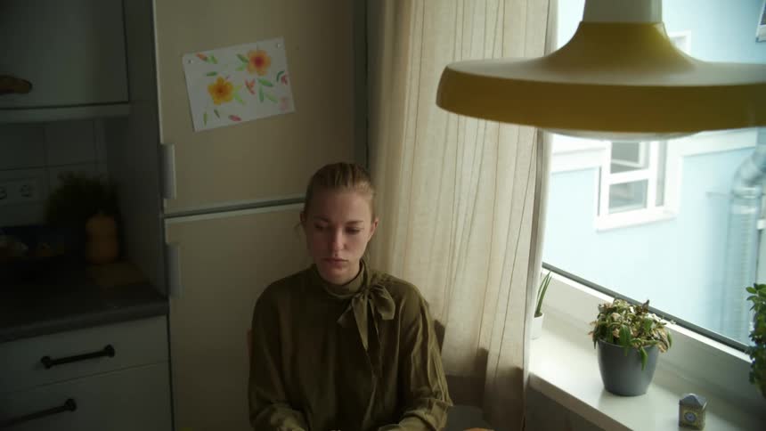 A woman in the kitchen sitting on a chair next to a table by the window