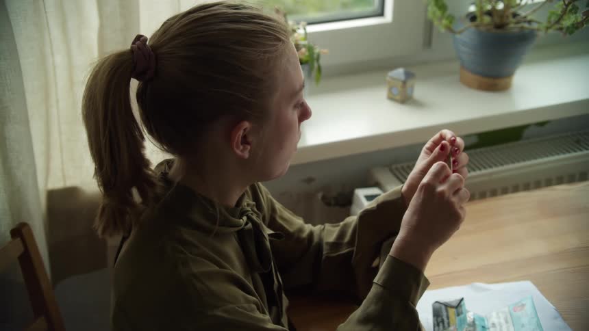 A woman sitting on a chair at a table rolling a cigarette next to a window