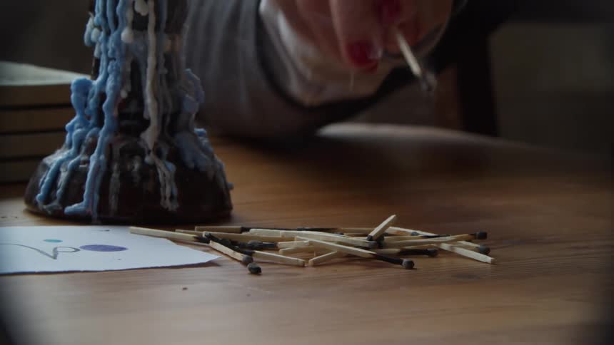 Woman lighting matches and piling them up over a table near a candle