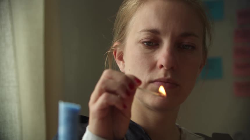 A woman sitting in a room lighting matches near her face at daytime