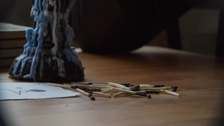 Woman lighting matches and piling them up over a table near a candle
