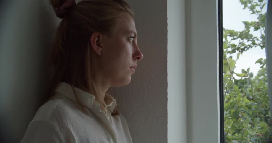 Nervous looking woman leaning against a wall looking out the window