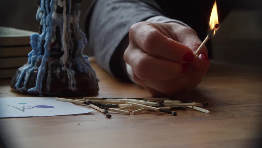 Woman lighting matches and piling them up over a table near a candle