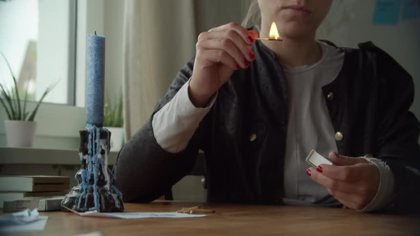 A young woman lighting matchsticks and blowing them out while sitting at an indoor table