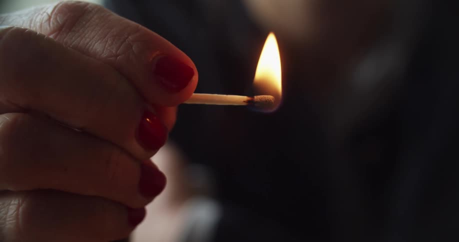 A woman lighting a match by striking it on the side of a matchbox