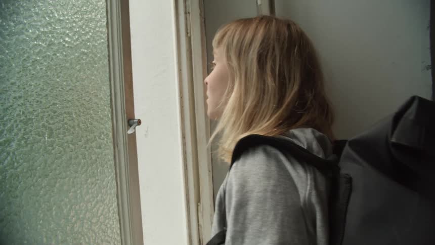 A teenager is looking out a window while wearing a backpack
