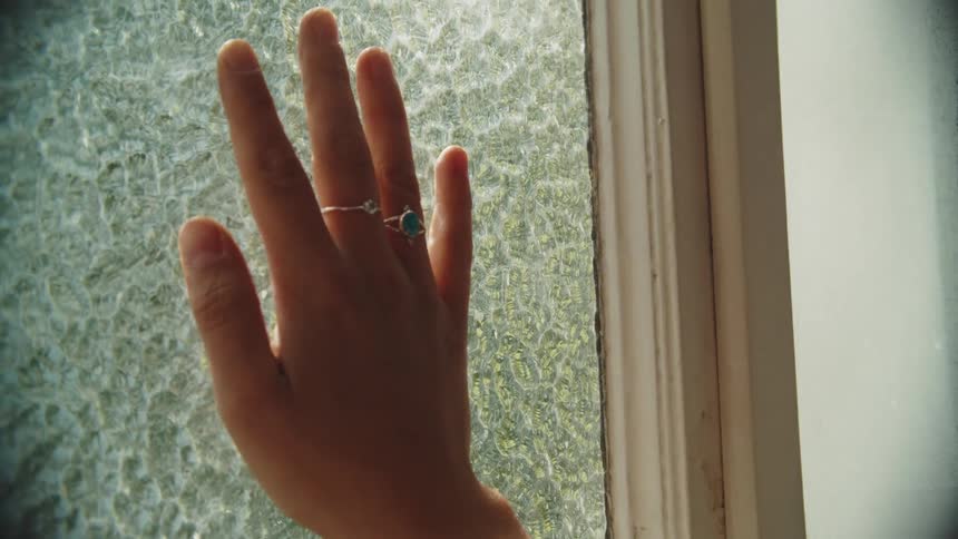 Hand pressing against a textured window indoors