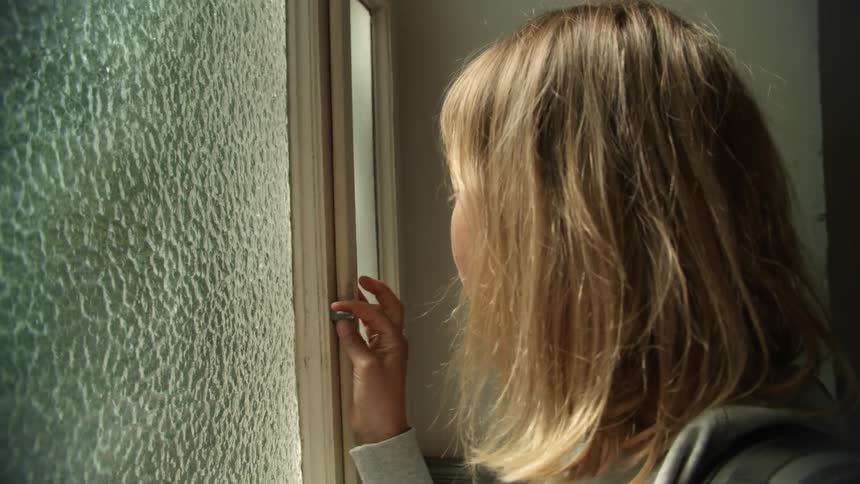 A teenage girl touching and opening a glass window