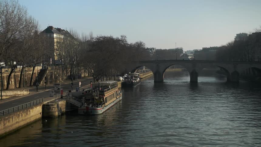 Ships floating dockside as a vehicle and pedestrians travel over a bridge in the background