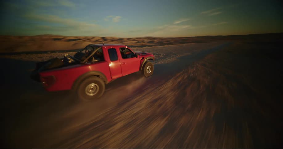 Orbiting aerial view of a red pickup truck driving in the desert kicking up dust at evening