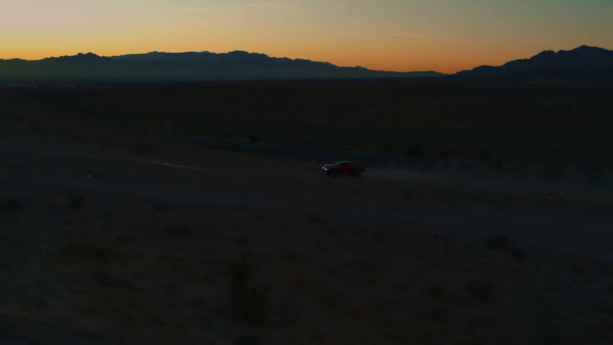 Long Tracking shot of racing truck driving through desert at sunset
