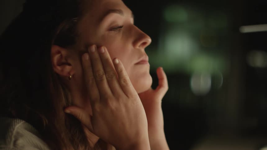 A woman puts her fingers over her eyes and pats her face and holds her hands in front of her face as she closes her eyes