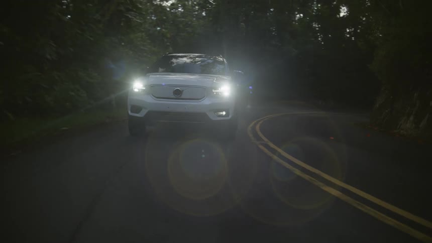 White car with headlights on driving on a road in the countryside at daytime
