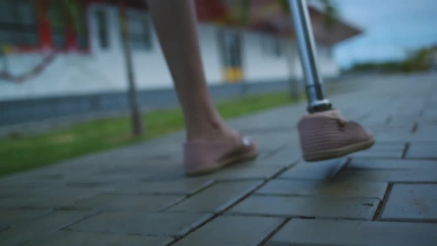 Close up of a woman with an artificial leg walking down a sidewalk in a neighborhood