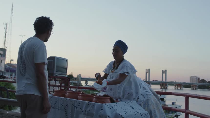 A woman on a dock serves a man typical Bahia, Brazil food acaraje