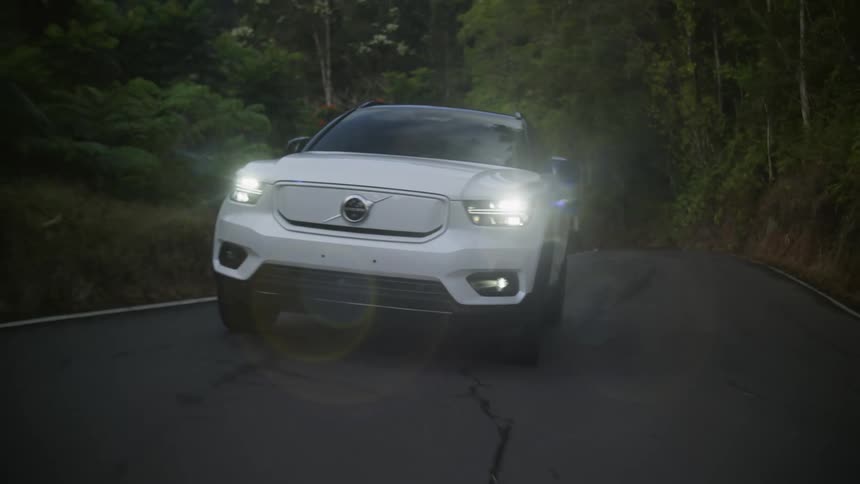White car with headlights on driving on a road in the countryside at daytime