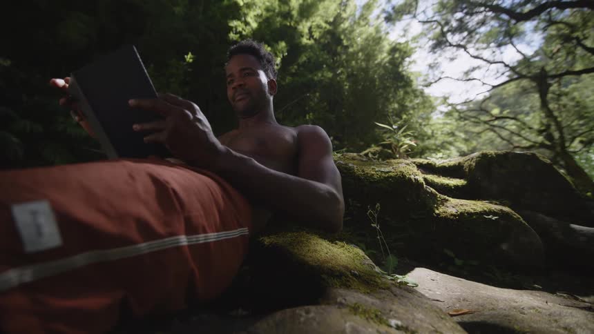 Topless man with red pants reads book in the jungle
