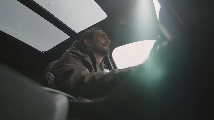 Man wearing jacket steers car with a sunroof