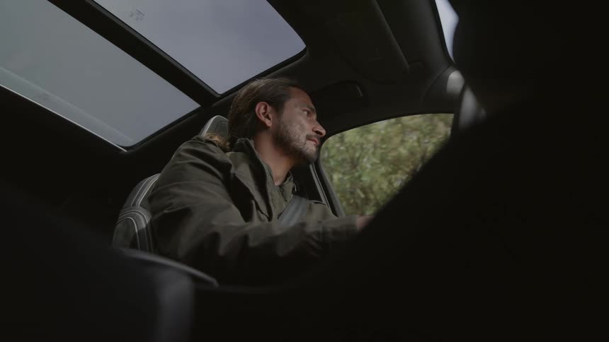 A man is driving an automobile with a sunroof and he looks around as he drives