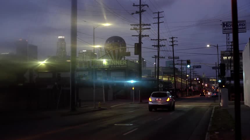 Vehicles travel along an urban street as night falls