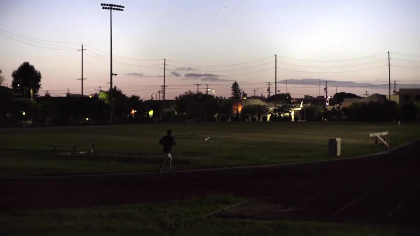 A person is running along the track of a field at dawn