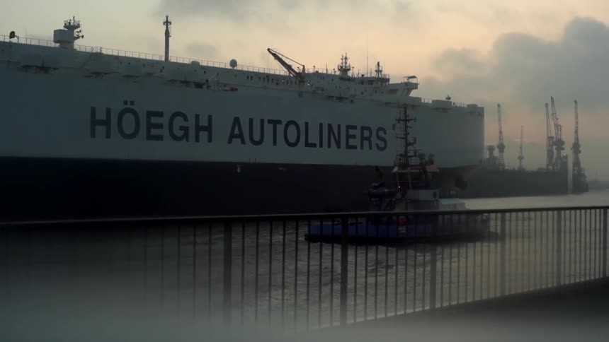 A boat travelling alongside a large freighter as it leaves a harbor