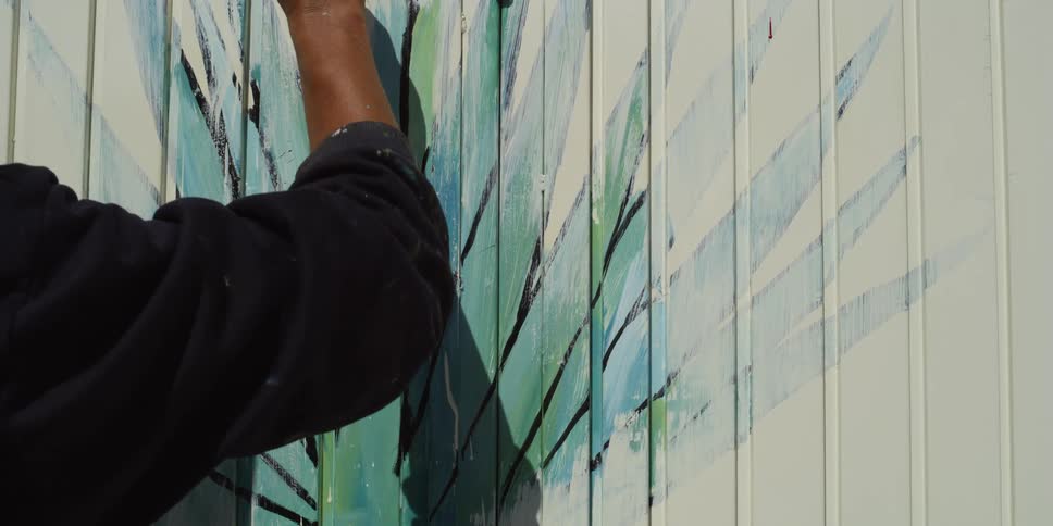 Artist paints a mural using a small brush at daytime