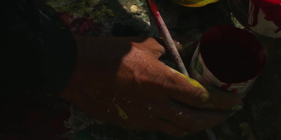 Close up of the hands of an artist stained in paint filling a container with red ink