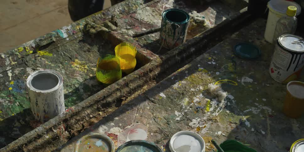 A man outside picks up paint and a paint brush and walks away