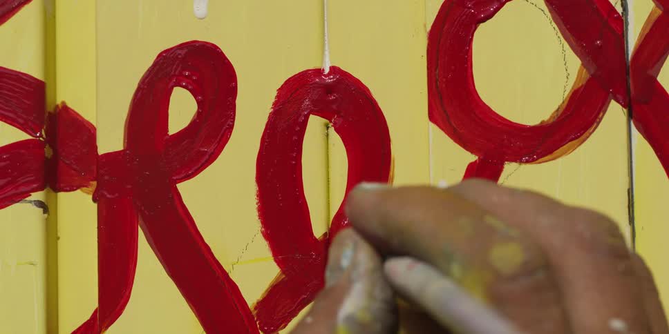 A man paints over a stenciled word on a sign