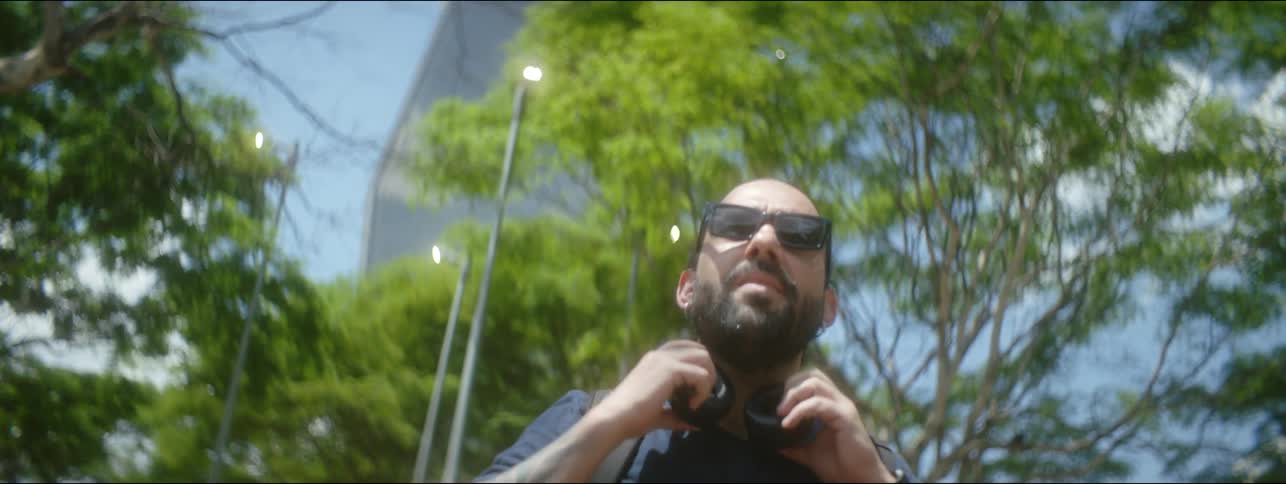 Man walking with skyscrapers in the background stops to remove his headphones