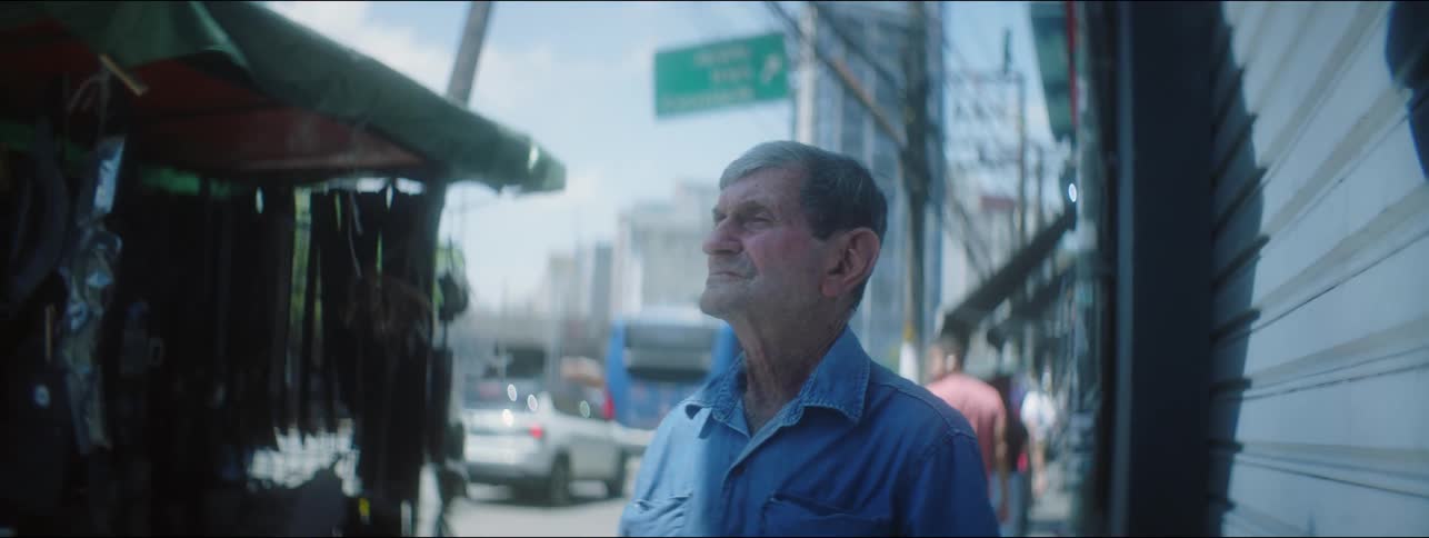 A man is looking up on a downtown sidewalk as people are walking and tall buildings are in the distance