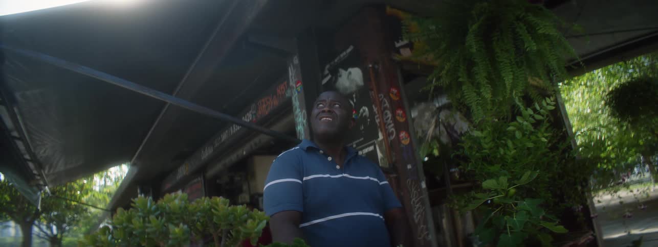 A smiling older black male standing outdoors in flower shop looks up surprised