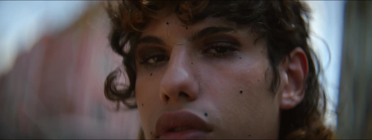 A non binary person stands next to a mural and faces the camera