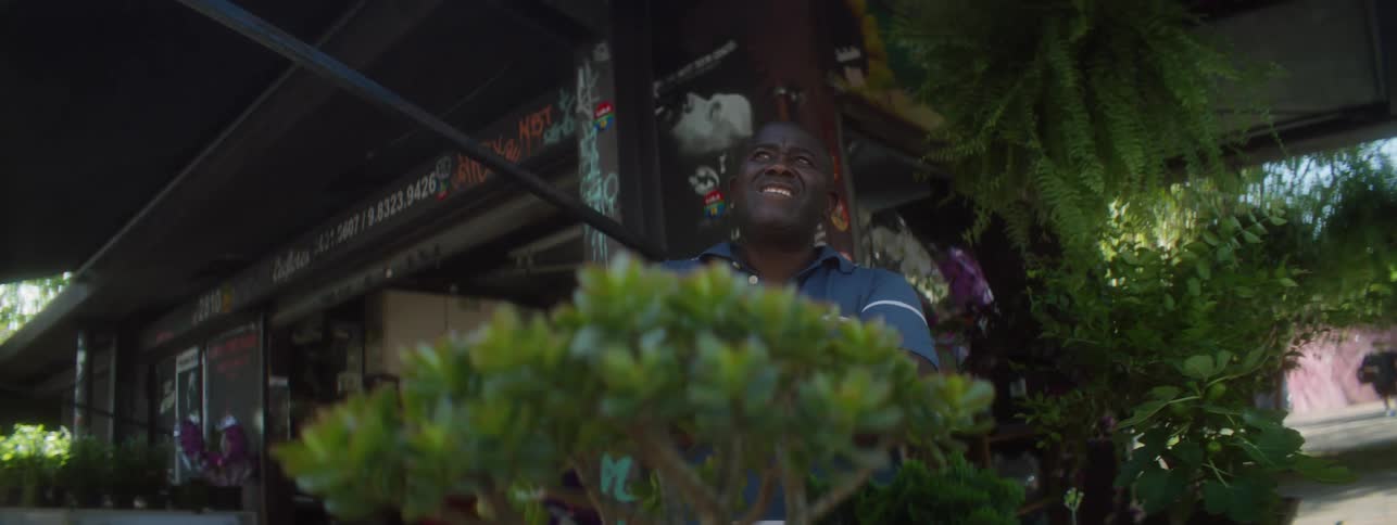 The sun shines brightly as a man stands in front of a business as he folds his arms with a smile on his face