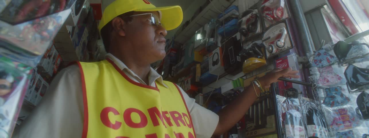 A man wearing a yellow hat and vest is standing in the doorway of his business looking outside