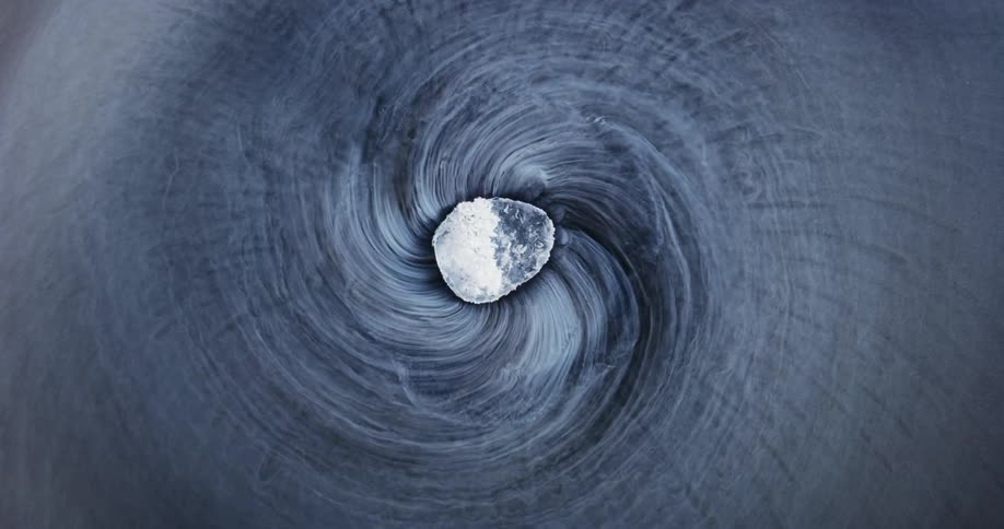 Brilliant rough gemstone spins as mixture underneath it spirals out in lines