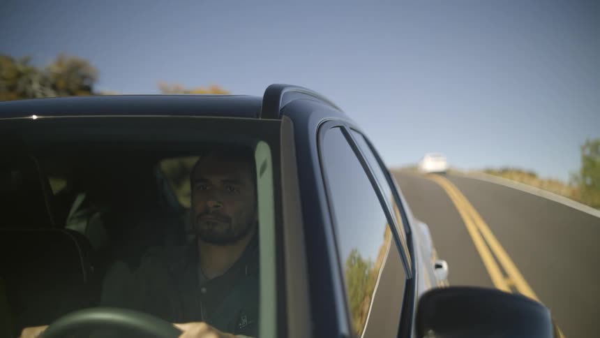 A man drives on a street as other cars drive on the other side of the road past him