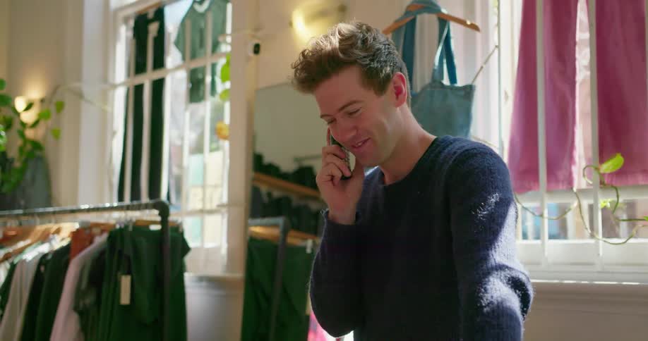Man in clothing store is talking and laughing on the phone