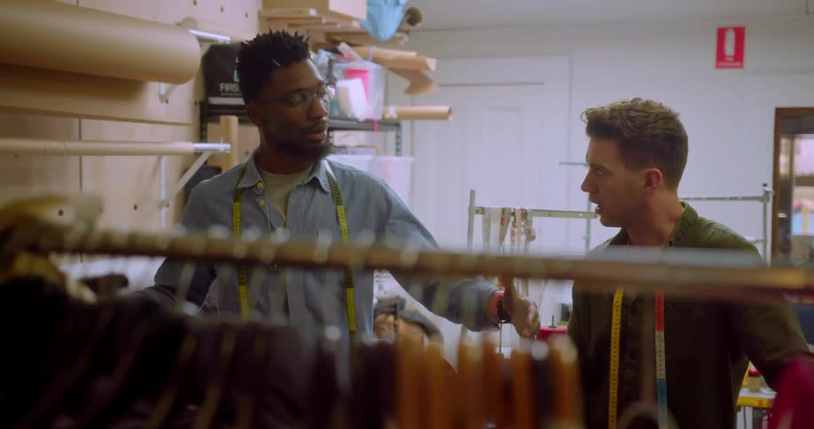 Two men converse in a clothes shop backroom