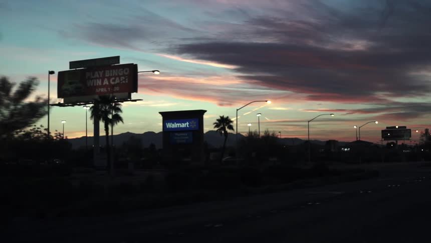 Lamp posts illuminate a road at dusk as vehicles drive