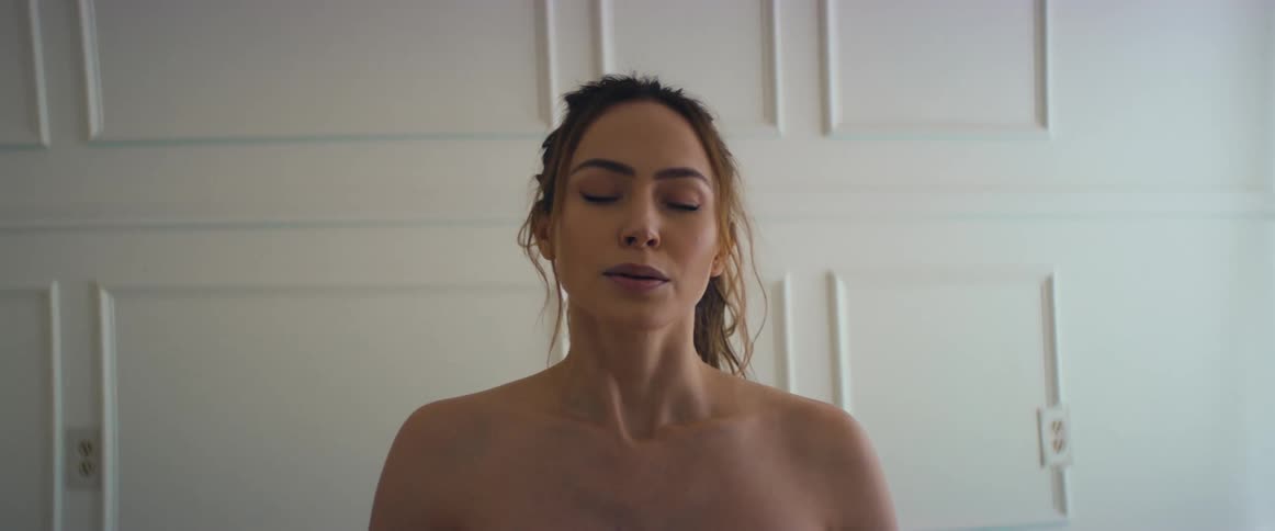 A woman with bare shoulders is standing in a room with her eyes closed and takes a deep breath and opens her eyes