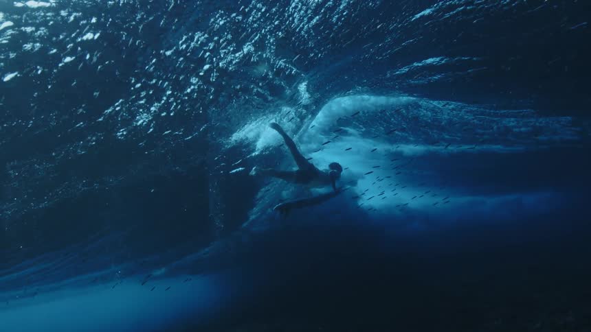 A man holds onto his surfboard while swimming under the sea