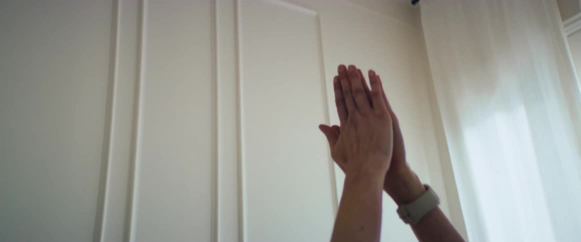 A woman sits at home and stretches her arms above her head while doing yoga