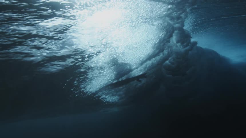 Underwater view looking up as a surfer rides a wave as it rolls overhead