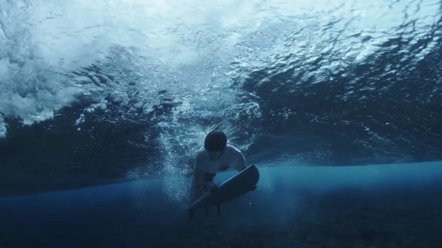 Male surfer with helmet holds surfboard and swims underwater
