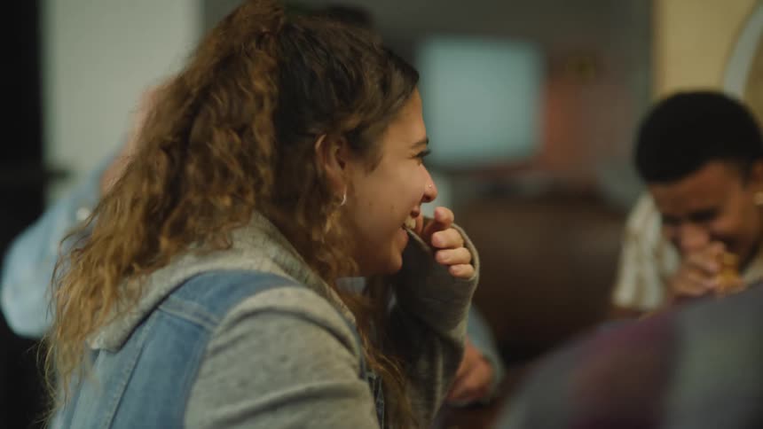A small group of people are sitting at a table talking and laughing as they eat pizza in a restaurant