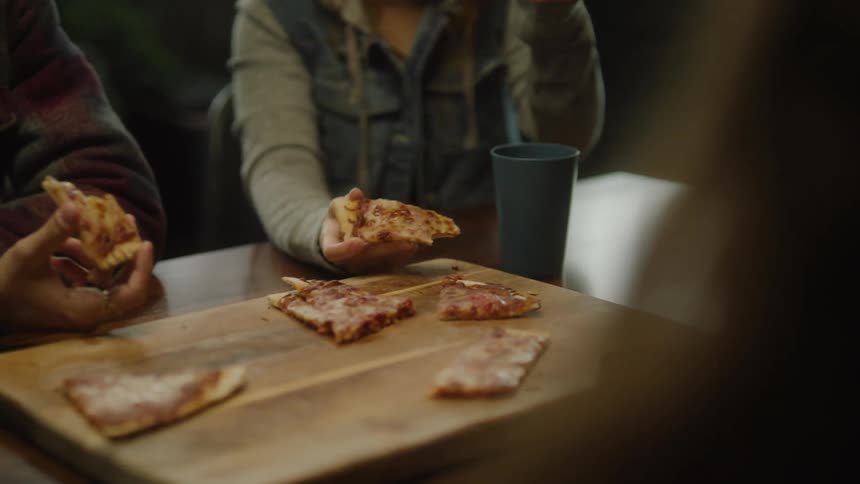 A small group of people are sitting at a table eating pizza at a restaurant